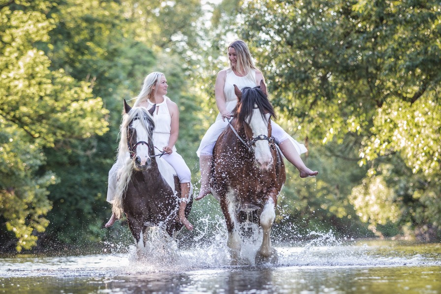 Zwei Freundinnen mit ihren beiden Pferden reiten durchs Wasser